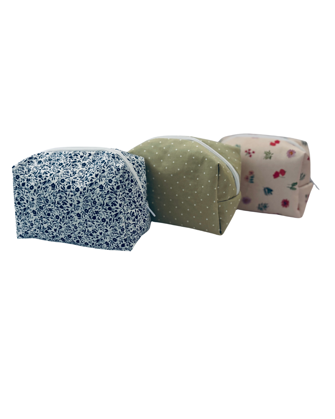 3 toiletry bags lined up. From left to right: mini navy floral, sage green polka dots, and pink scattered floral print. Set against a white background.