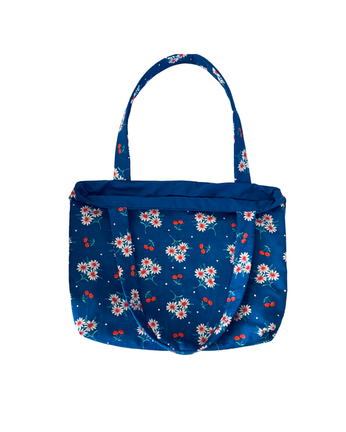 blue tote bag with red cherry and white floral print with blue interior against a white background